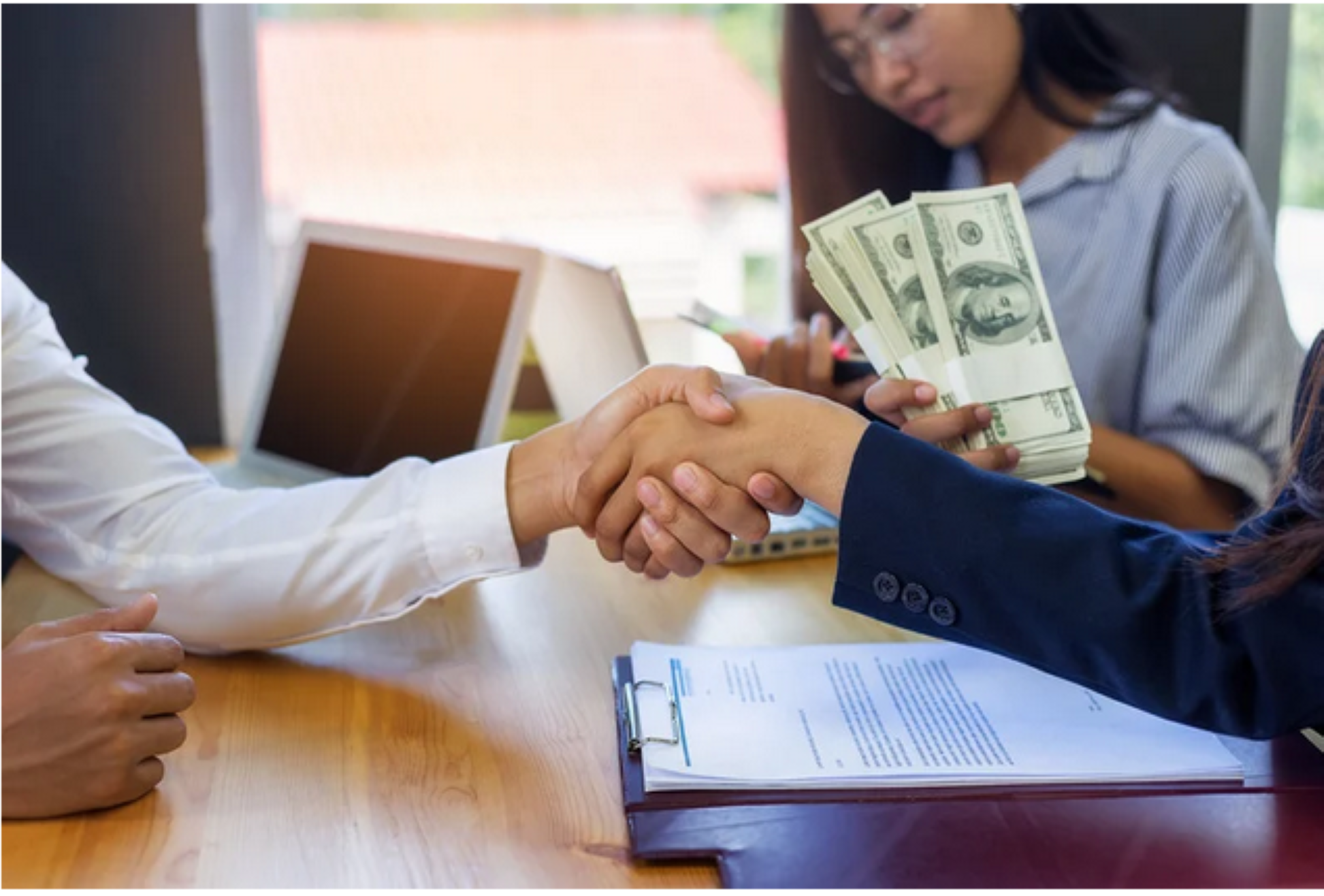 two people shaking hands and displaying cash